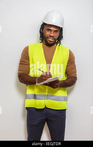A construction worker in a reflective vest and hard hat confidently takes notes on a white background. Stock Photo