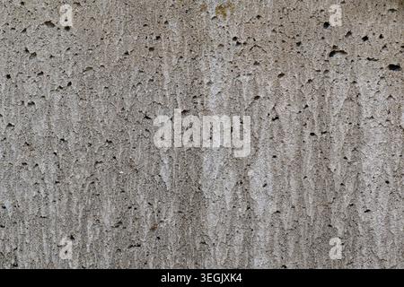 Close-up texture of a rough gray concrete wall with porous surface details, subtle vertical marks, and natural imperfections Stock Photo