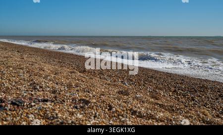 Pebble beach shoreline with incoming waves under clear blue sky. Stock Photo
