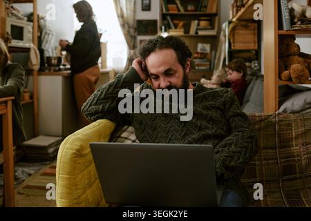 Middle Aged Man Using Laptop in Crowded Home during Financial Hardship Stock Photo