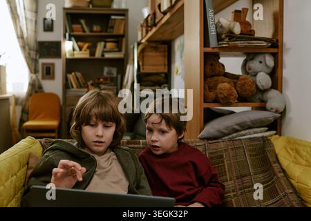Two Boys Using Laptop at Home for Online Learning and Research Stock Photo