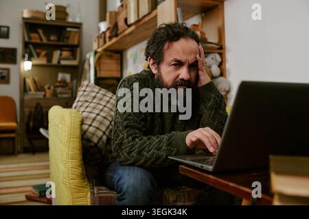 Middle Aged Man Working on Laptop with Financial Stress at Home Stock Photo