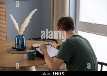 Young man studying with digital tablet at dining table in modern home interior during daytime Stock Photo