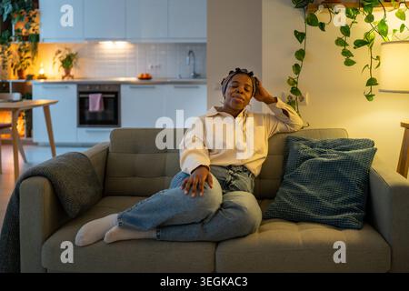 Serene smiling black woman sleeping leaned on soft sofa cushions taking nap break after fruitful day Stock Photo