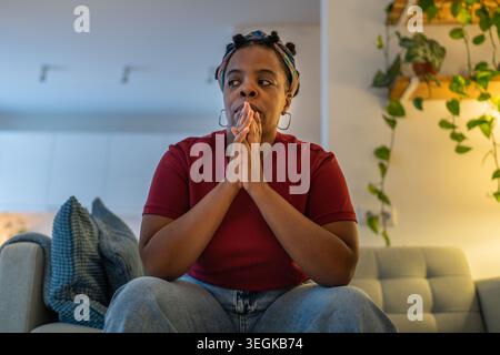 Anxious stressed black woman sitting on couch at home thinks about difficult unresolved challenges.  Stock Photo
