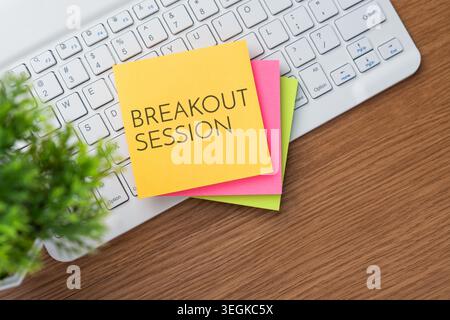 White computer keyboard on a wooden desk and colorful sticky notes with text BREAKOUT SESSION. Corporate meetings, team collaboration concept. Stock Photo