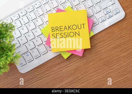 White computer keyboard on a wooden desk and colorful sticky notes with text BREAKOUT SESSION. Corporate meetings, team collaboration concept. Stock Photo
