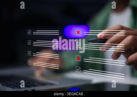 Hand using stylus pen to evaluate checklist on laptop. Businessman checking boxes with tick and cross marks for quality control, survey, and business Stock Photo