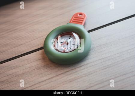 Portable green and orange compass on a wooden table, suitable for travel use and practical field tasks.  Stock Photo