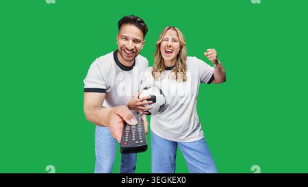 A man and a woman are switching on a soccer game using the remote control on the TV. Watch live stream soccer and sports at home. Stock Photo