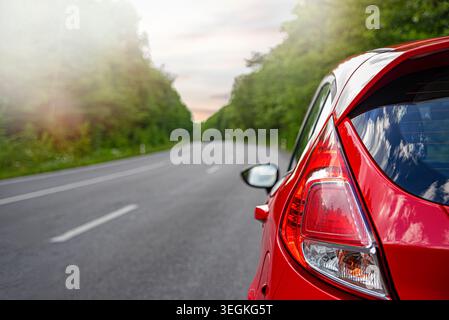 A red car is parked on the side of an empty asphalt road. Stock Photo