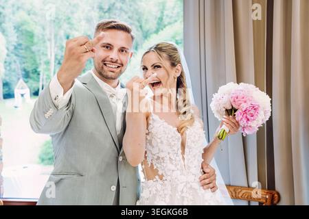 happy, laughing bride and groom at the wedding. Bride and groom cheekily show the rings on their middle or ring fingers to the camera. Stock Photo
