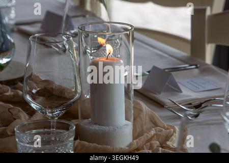 Lit candle in glass hurricane creating warm ambiance on elegantly set dining table Stock Photo