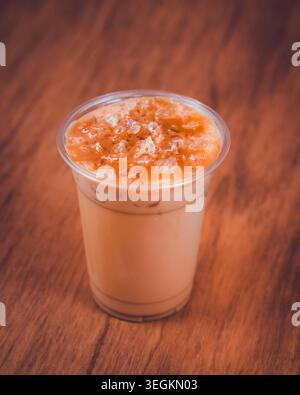 Iced milk tea with crushed ice in a clear plastic cup on a wooden table Stock Photo