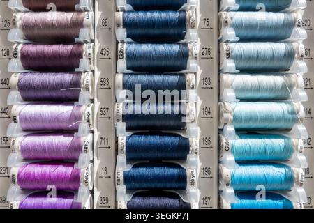 Colorful sewing thread spools in various shades of blue are neatly organized in a display rack, representing creativity and craft supplies for textile Stock Photo