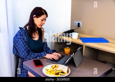 Woman working remotely during breakfast morning routine Stock Photo