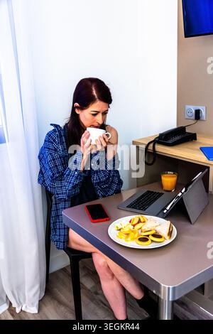 Woman working remotely during breakfast routine at hotel Stock Photo