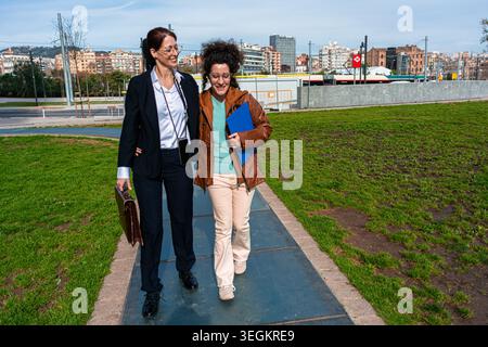Businesswomen walking together through urban park discussing work Stock Photo