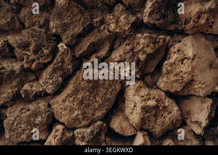 Rough limestone rocks stacked in natural wall texture with dark earthy tones porous mineral surface rugged geology background organic stone pattern Stock Photo