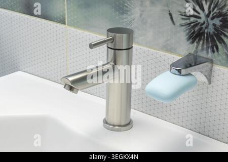 White ceramic bathroom sink with modern chrome faucet and blue soap on a wall-mounted holder Stock Photo