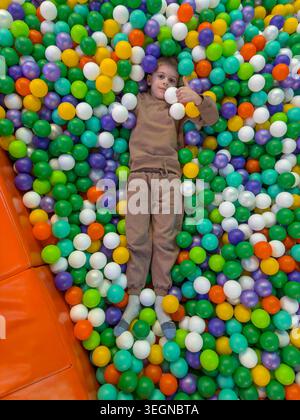 Boy lying in dry ball pit with bright colorful plastic balls. Stock Photo