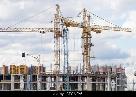 Tower cranes actively constructing a modern residential building, featuring intricate scaffolding and formwork, representing continuous urban development and architectural progress Stock Photo