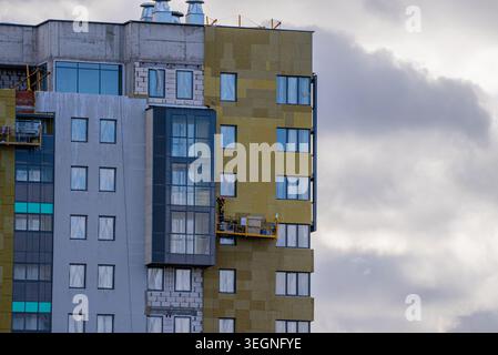 Modern high-rise apartment building undergoing exterior construction, workers on a suspended platform installing thermal insulation materials on the facade for energy efficiency Stock Photo