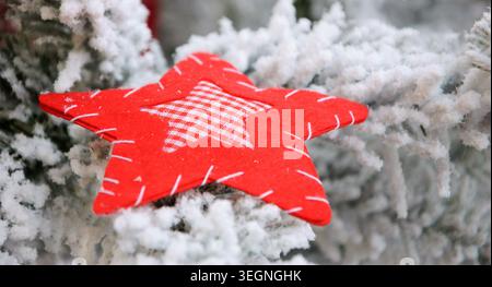 Rustic handmade red star ornament with checked center and artificial snow on Christmas tree branches Stock Photo