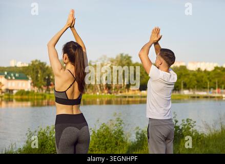 Relaxed sporty young couple with raised arms standing in prayer pose and practicing yoga outdoors. Stock Photo