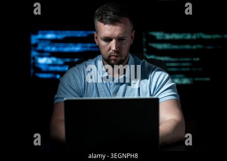 Hacker works on computer with focus. Hacker analyzes digital code in darkness. Hacker monitors network traffic activity. Hacker creates malware for Stock Photo