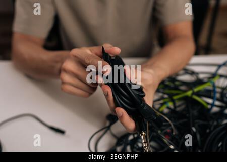 Close-up hand of unrecognizable man achieving success organizing messy technology cables, holding a neatly coiled cord after managing frustration from Stock Photo