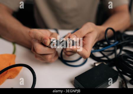 Audio technician hands holding xlr microphone cable, connecting male and female audio jacks, surrounded by tangled wires and various sound equipment Stock Photo