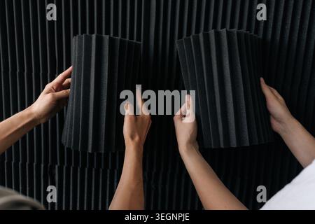 Close-up of handyman installing black acoustic foam panels on a studio wall, creating a professional soundproofing setup for improved sound absorption Stock Photo