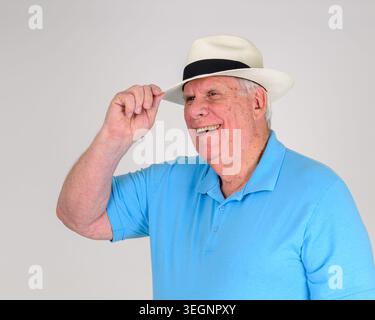 Man wears a light Panama straw hat with a black band. His bright blue polo shirt appears casual and fresh. He smiles warmly while tipping his hat. The Stock Photo