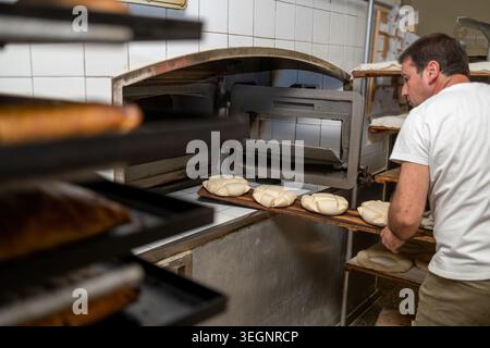 Baker placing fresh dough shaping into a hot oven Stock Photo