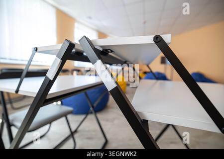 Close-up view of modern adjustable school study desks with white tops and black metal frames arranged in an empty classroom setting with blue and yell Stock Photo