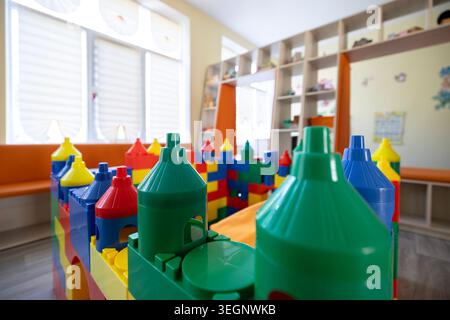 A close-up view of a multicolored toy castle constructed from large plastic building blocks in a brightly lit daycare playroom with shelves, large win Stock Photo