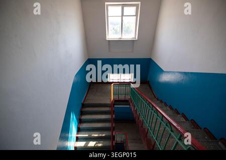 An interior high angle view of an empty concrete staircase inside a residential or public building with white and blue painted walls, green metal rail Stock Photo