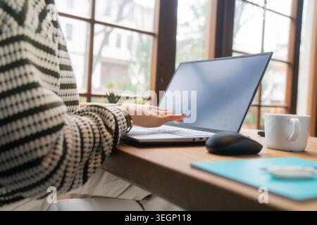 Aesthetic home office scene featuring female hands operating a laptop with empty screen. Comfortable remote working environment with modern technology Stock Photo