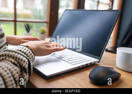 Close-up image of a woman opening and using a modern laptop computer at a cozy home office desk. Stylish remote working environment with wireless mous Stock Photo