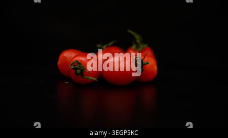 Ripe cherry tomatoes hanging on vine spinning slowly against dark backdrop, showcasing vibrant red color and fresh organic produce with pristine visua Stock Photo