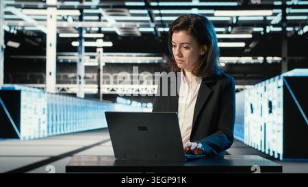 Data center engineer typing on laptop keyboard to troubleshoot supercomputers connectivity issues. Server hub expert using program on notebook to analyze system logs, fixing gear errors Stock Photo