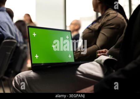 Green screen laptop during debate in conference room with chairs filled by business professionals. Diverse audience group listening closely to guest speaker, encouraging engagement. Stock Photo