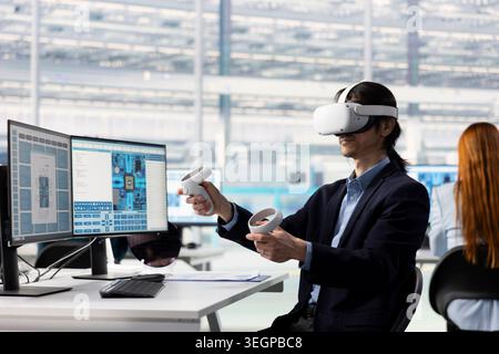 Asian man testing microchip electronics prototypes using VR tech. Senior manager wearing virtual reality goggles ensures industrial hardware standards in semiconductors RD laboratory Stock Photo