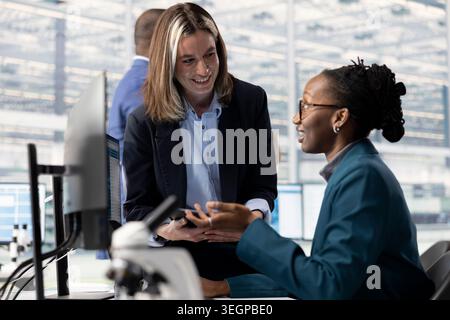 Observing microchip layout, microscope and African american woman with manager in RD office. Doing innovative study, microscopy tool and teamworking colleagues researching materials Stock Photo