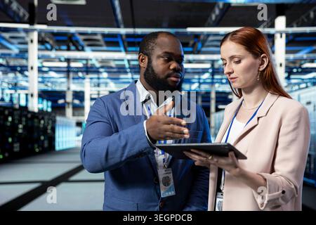Data center coworkers using tablet app to manage equipment systems used for database storage. IT staff members working together in high tech industry 4.0 server farm, technology concept Stock Photo