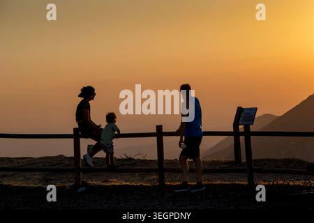 Three people, a father with a girl and a boy standing while watching sun setting behind distant mountain peaks, Peña de Francia, Salamanca, Spain Stock Photo