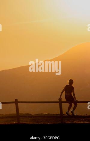 Three people, a father with a girl and a boy standing while watching sun setting behind distant mountain peaks, Peña de Francia, Salamanca, Spain Stock Photo