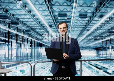 Portrait of smiling man in microchip factory using laptop to manage resource allocation. Happy director analyzing industry 4.0 semiconductor plant operations efficiency from elevated platform Stock Photo
