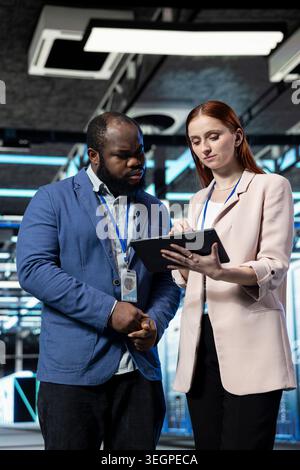 Managing equipment, tablet app and coworkers in data center with database storage systems. Working together, technology concept and IT staff members in high tech industry 4.0 server farm Stock Photo